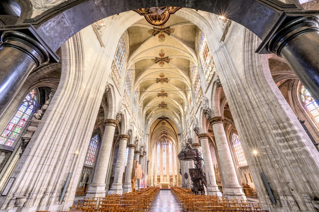 View of the interior of a cathedral with vaults, columns and stained glass windows.